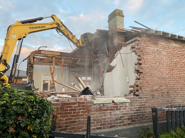 Digger demolishing an old brick house